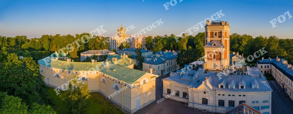 На фотографии запечатлён Екатерининский дворец в Царском Селе — великолепный образец русского барокко. Рядом расположены исторические постройки, окружённые зеленью парка, что создаёт атмосферу гармонии между архитектурой и природой. Летнее утро освещает дворец и прилегающие здания, придавая им мягкие тёплые оттенки. Этот ансамбль является одной из главных достопримечательностей Санкт-Петербурга и его окрестностей, привлекая туристов со всего мира.
